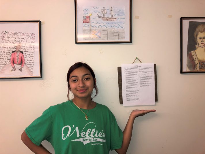 student displaying written work on wall