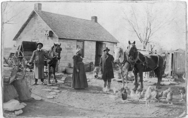 This black and white photograph shows John Summer and his family standing in front of their home located two miles northeast of Dunlap, Morris County, Kansas. The home was built in the 1880s.