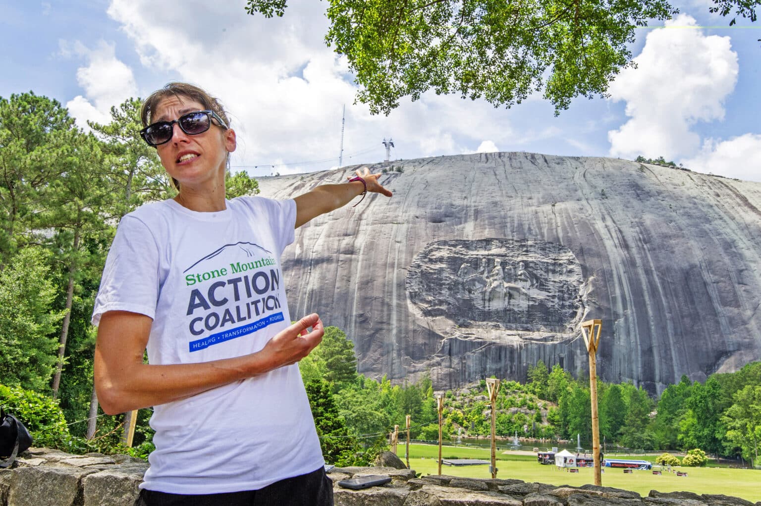 woman in t-shirt points to Stone Mountain behind her
