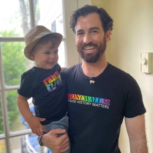 man in Stonewall 50 shirt with smiling baby in hat